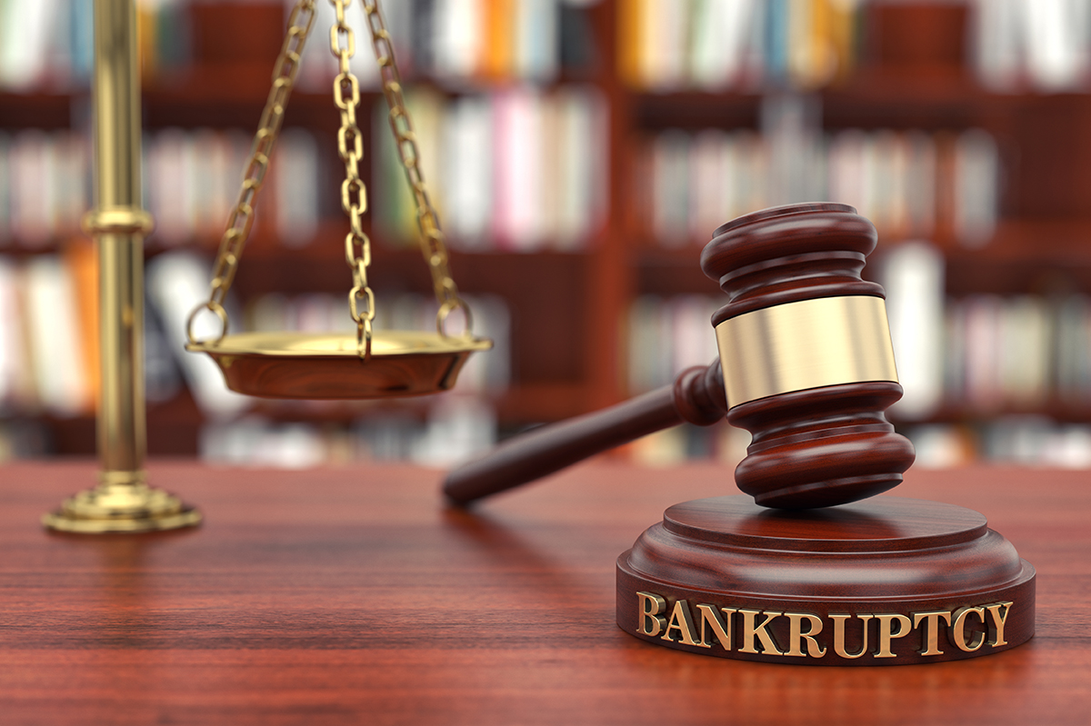 Bankruptcy law concept, judge's gavel with "BANKRUPTCY" on it next to the scales of justice (brass scales), on lawyer's desk.
