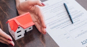 Hands near house model, bankruptcy paperwork and pen on table