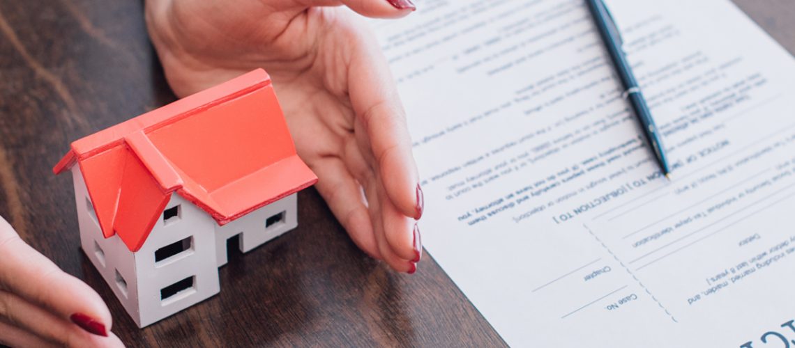 Hands near house model, bankruptcy paperwork and pen on table